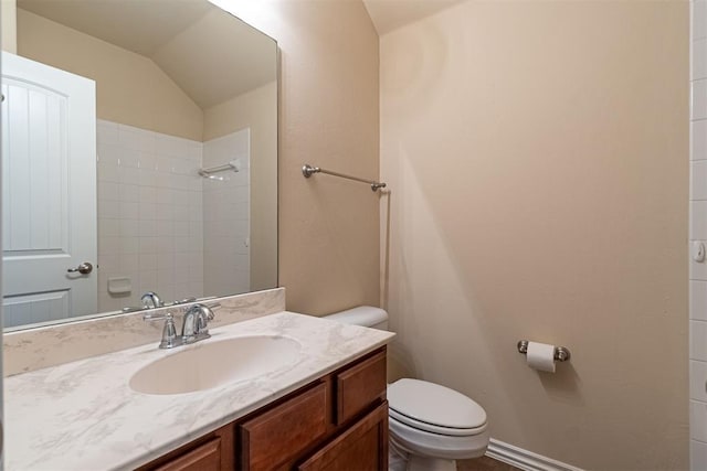 bathroom featuring vanity, toilet, lofted ceiling, and tiled shower