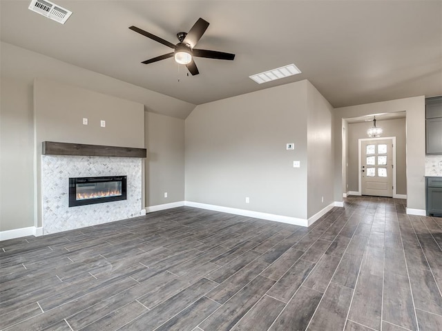 unfurnished living room featuring lofted ceiling, a fireplace, and ceiling fan with notable chandelier