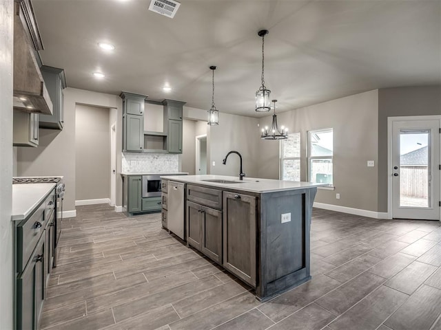 kitchen with sink, plenty of natural light, an island with sink, decorative backsplash, and decorative light fixtures