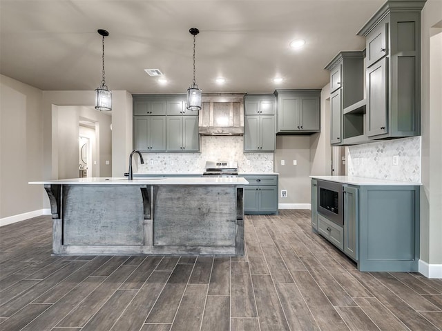 kitchen featuring a kitchen breakfast bar, an island with sink, pendant lighting, stainless steel appliances, and wall chimney range hood