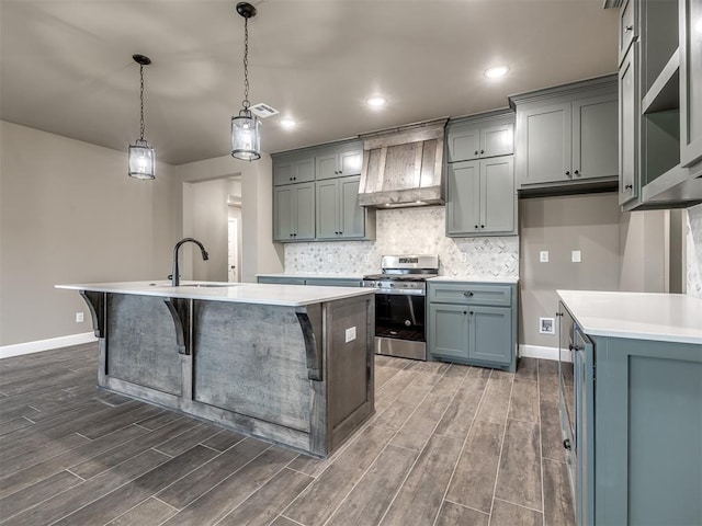 kitchen featuring sink, hanging light fixtures, stainless steel range with gas stovetop, custom range hood, and a center island with sink