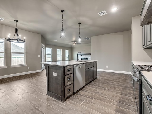 kitchen featuring sink, a kitchen island with sink, stainless steel appliances, dark brown cabinetry, and decorative light fixtures