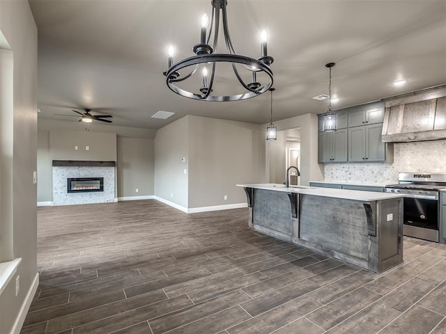 kitchen featuring gas stove, hanging light fixtures, a center island with sink, ceiling fan with notable chandelier, and backsplash