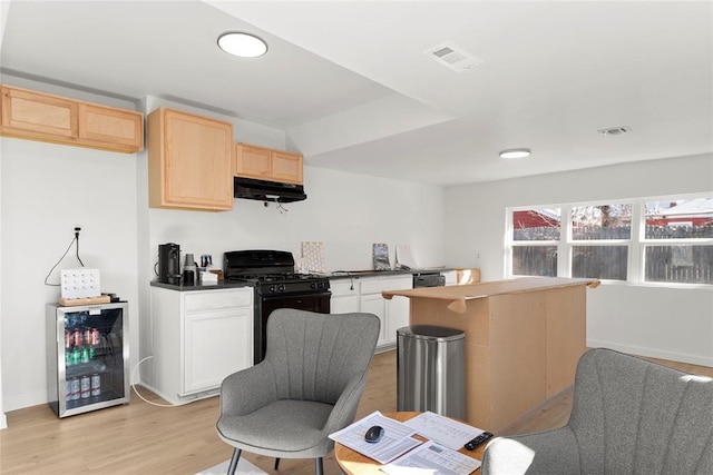 kitchen featuring visible vents, under cabinet range hood, wine cooler, black gas range oven, and light wood-style floors