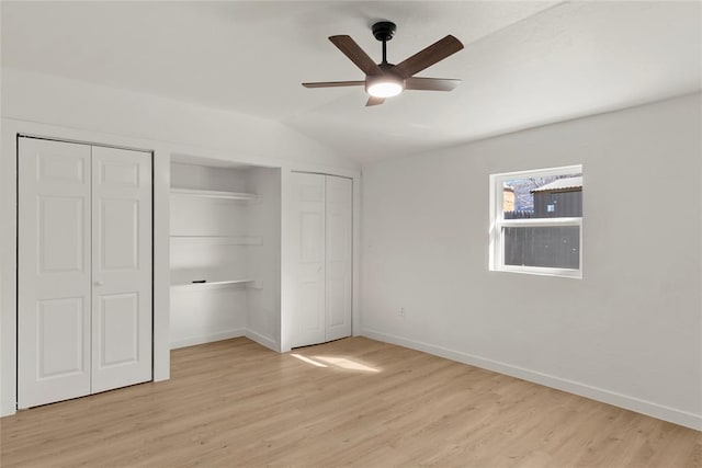 unfurnished bedroom with a ceiling fan, baseboards, lofted ceiling, light wood-style floors, and multiple closets