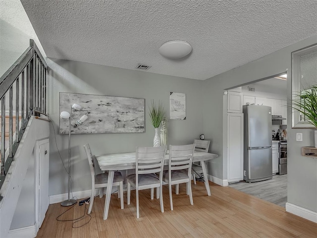 dining space with light wood-type flooring and a textured ceiling