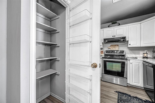 kitchen with light stone countertops, appliances with stainless steel finishes, white cabinetry, and wood-type flooring