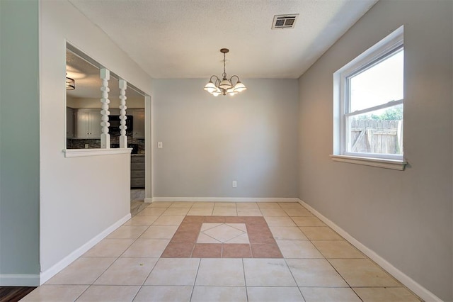 spare room featuring light tile patterned floors, a textured ceiling, and a chandelier