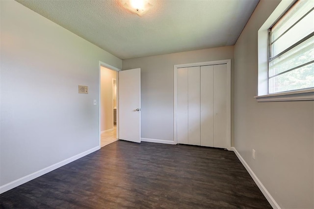 unfurnished bedroom with a textured ceiling, dark wood-type flooring, and a closet