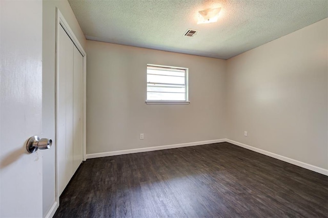 unfurnished bedroom featuring a textured ceiling, a closet, and dark wood-type flooring