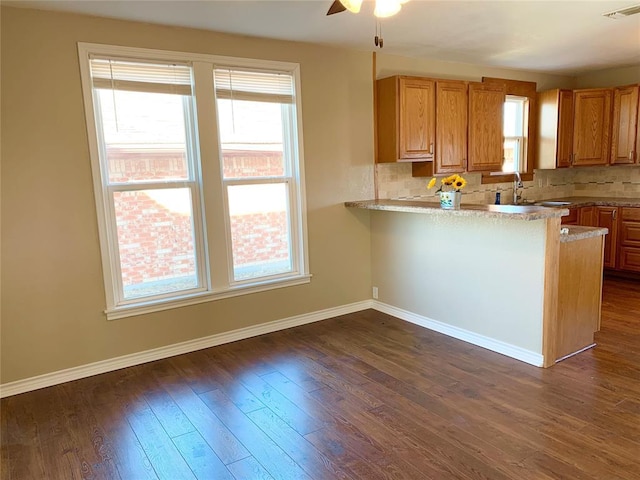 kitchen with kitchen peninsula, ceiling fan, backsplash, dark wood-type flooring, and sink