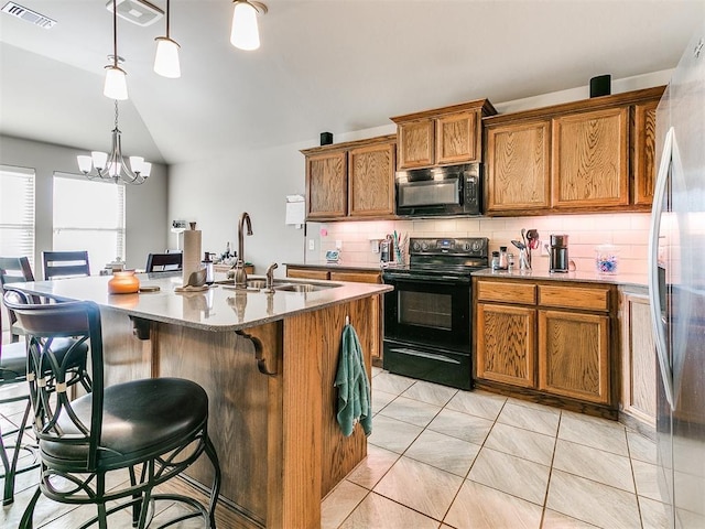 kitchen with tasteful backsplash, black appliances, decorative light fixtures, a notable chandelier, and an island with sink