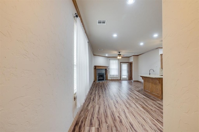 unfurnished living room with ceiling fan, sink, light wood-type flooring, and ornamental molding