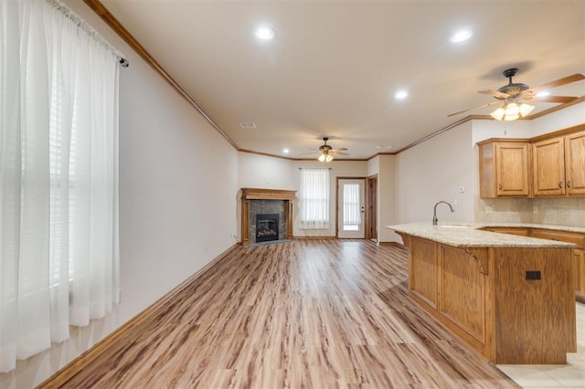 kitchen with ceiling fan, light stone countertops, light hardwood / wood-style flooring, crown molding, and a kitchen bar