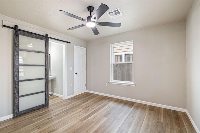 unfurnished bedroom featuring ceiling fan, a barn door, and light wood-type flooring