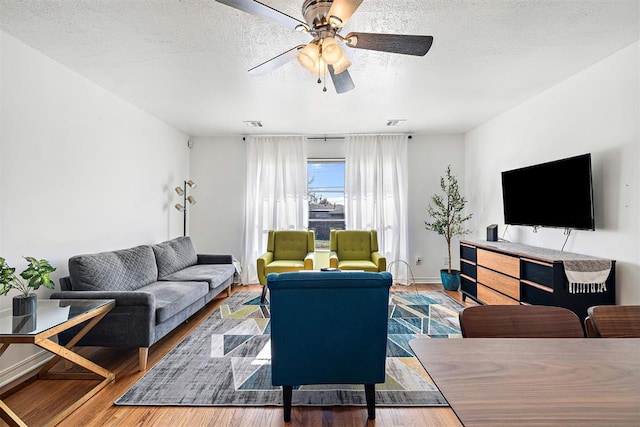 living room with ceiling fan, wood-type flooring, and a textured ceiling