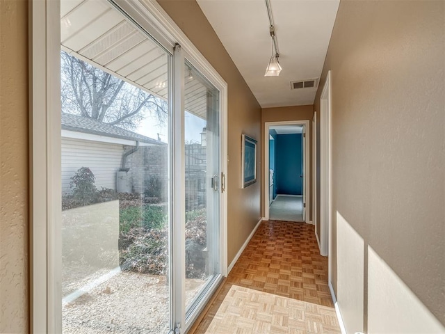 doorway to outside with baseboards, visible vents, and track lighting