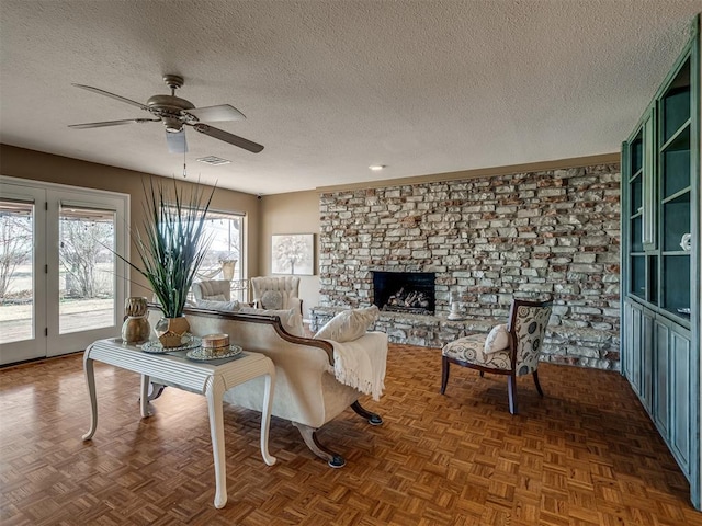 living area with a textured ceiling, a fireplace, visible vents, and a ceiling fan