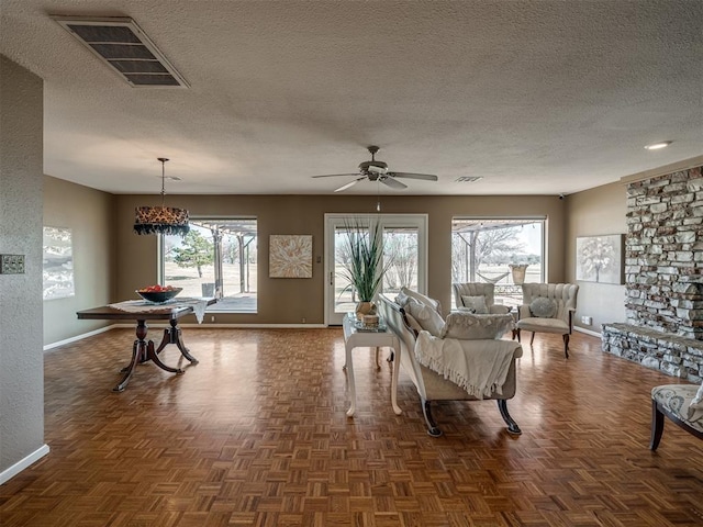 living room with a ceiling fan, baseboards, visible vents, and a textured ceiling