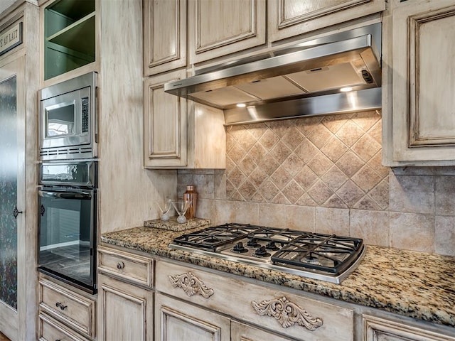 kitchen with appliances with stainless steel finishes, decorative backsplash, light stone counters, and range hood