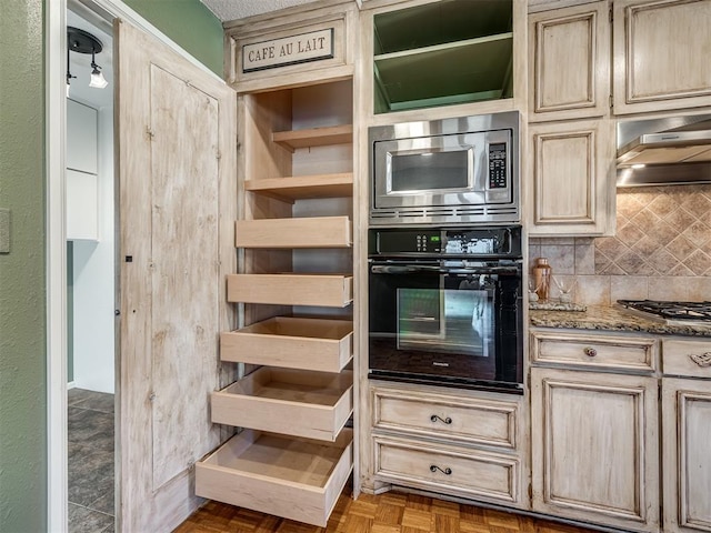 kitchen with stone counters, stainless steel microwave, decorative backsplash, oven, and under cabinet range hood