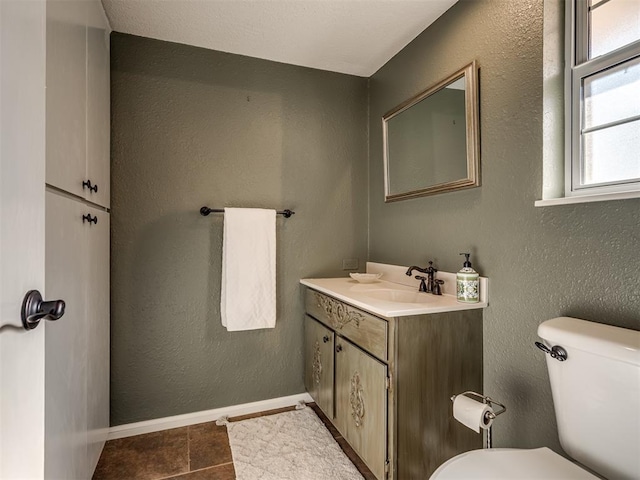 bathroom with a textured wall, vanity, and toilet