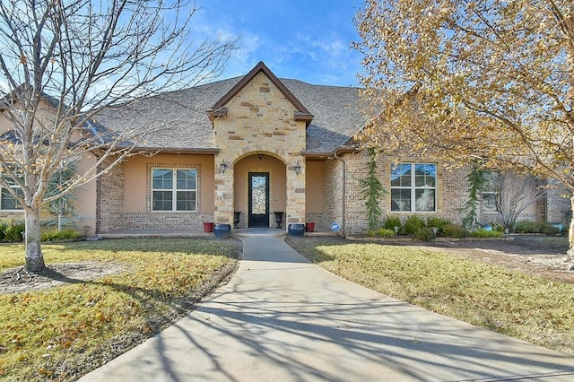 view of front facade featuring stone siding, brick siding, roof with shingles, and a front yard