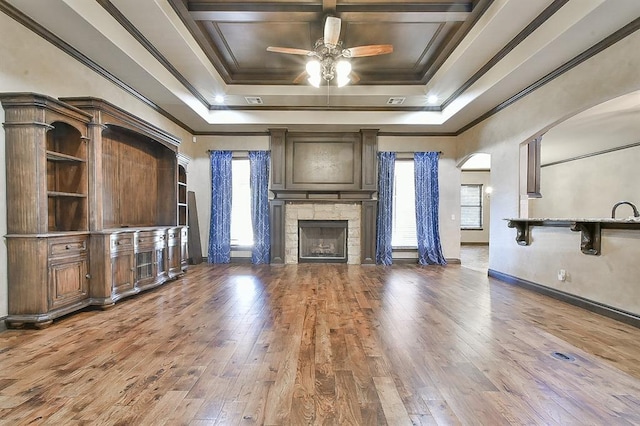 unfurnished living room featuring arched walkways, a raised ceiling, wood finished floors, crown molding, and a fireplace