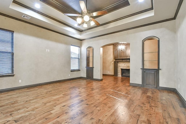 unfurnished living room featuring arched walkways, a raised ceiling, visible vents, ornamental molding, and wood finished floors