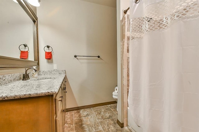 bathroom with stone finish floor, toilet, vanity, and baseboards