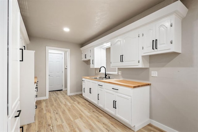 kitchen with wood counters, light hardwood / wood-style floors, white cabinetry, and sink