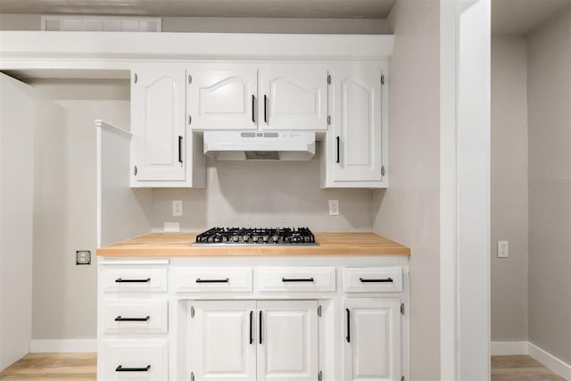 kitchen with white cabinets, stainless steel gas stovetop, butcher block countertops, and light hardwood / wood-style flooring