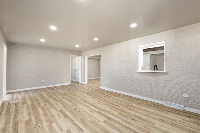 unfurnished room featuring light hardwood / wood-style floors and brick wall