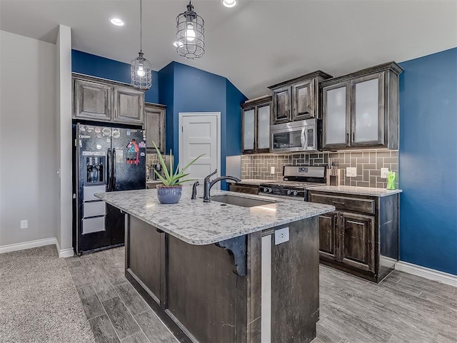 kitchen with decorative backsplash, appliances with stainless steel finishes, sink, pendant lighting, and a center island with sink