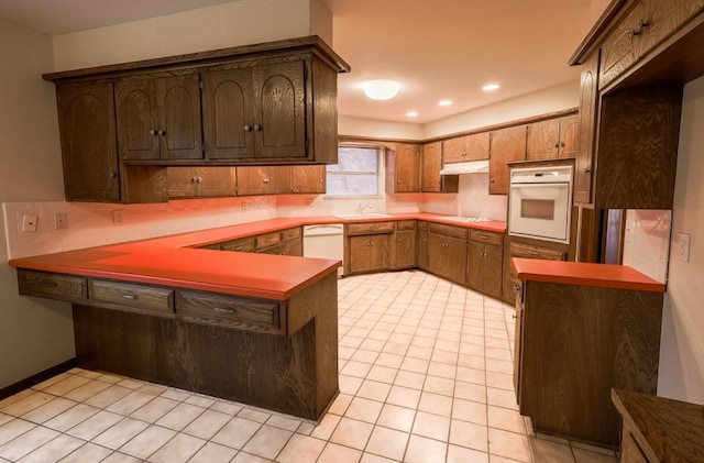 kitchen with light tile patterned flooring, white appliances, kitchen peninsula, and sink