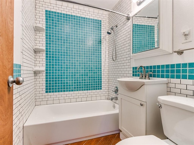 full bathroom with tiled shower / bath, vanity, tile walls, and toilet