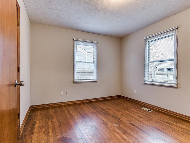 empty room with wood-type flooring, a textured ceiling, and a healthy amount of sunlight