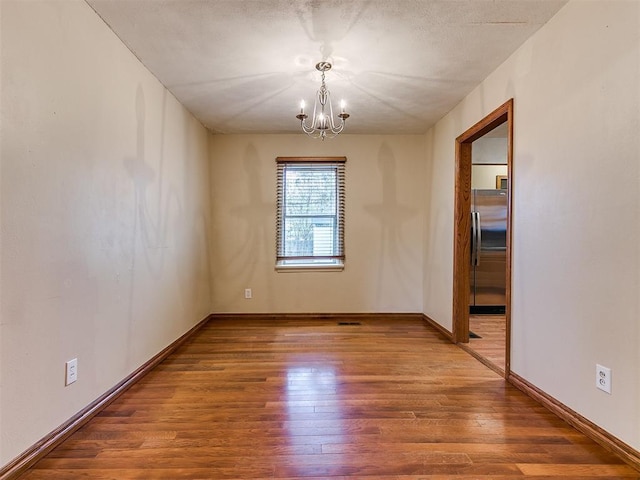 spare room with an inviting chandelier and hardwood / wood-style flooring