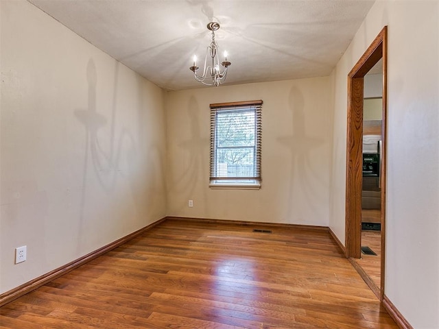 spare room featuring hardwood / wood-style floors and a notable chandelier