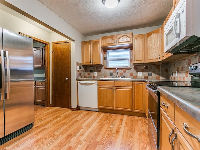 kitchen featuring tasteful backsplash, a textured ceiling, stainless steel appliances, sink, and light hardwood / wood-style flooring