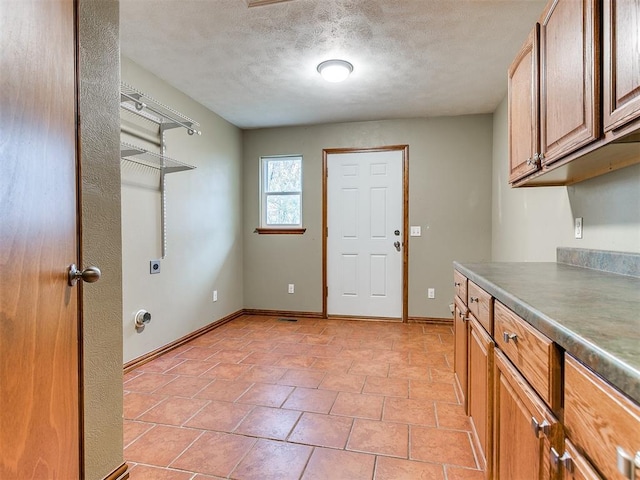 washroom with electric dryer hookup, light tile patterned flooring, cabinets, and a textured ceiling