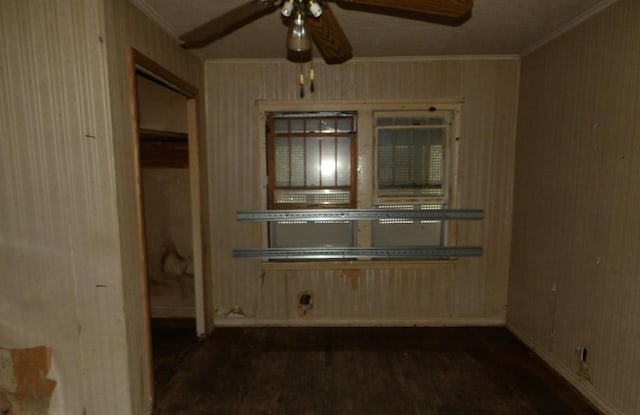 interior space featuring ceiling fan, ornamental molding, dark wood-type flooring, and wooden walls