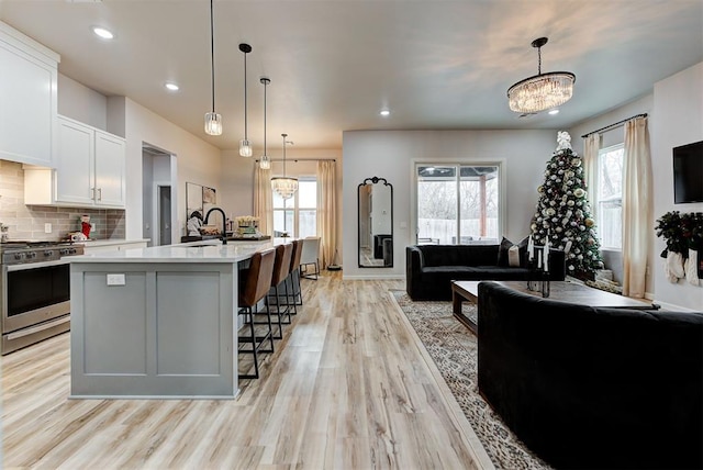 kitchen with gas range, light wood-type flooring, an island with sink, decorative light fixtures, and white cabinetry