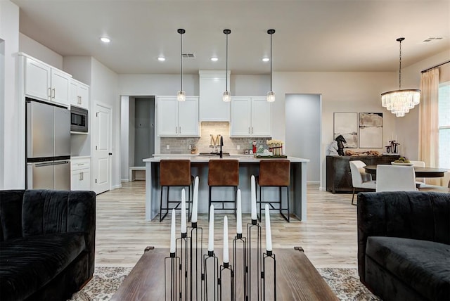 kitchen featuring a kitchen bar, appliances with stainless steel finishes, white cabinets, hanging light fixtures, and an island with sink