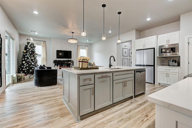 kitchen with sink, light hardwood / wood-style floors, pendant lighting, a center island with sink, and appliances with stainless steel finishes