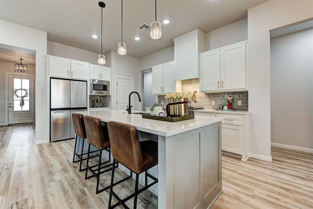 kitchen featuring sink, light hardwood / wood-style floors, a kitchen island with sink, white cabinets, and appliances with stainless steel finishes