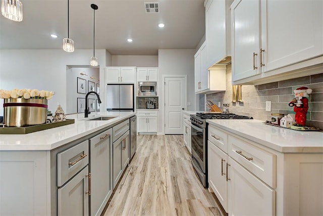 kitchen with white cabinets, a center island with sink, sink, light hardwood / wood-style flooring, and appliances with stainless steel finishes