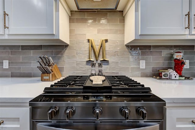 interior details featuring decorative backsplash, stove, white cabinetry, and light stone counters