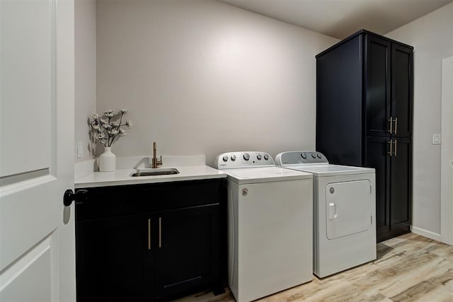 clothes washing area featuring cabinets, washing machine and dryer, light hardwood / wood-style flooring, and sink