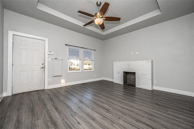 unfurnished living room featuring a fireplace, a raised ceiling, ceiling fan, and dark wood-type flooring